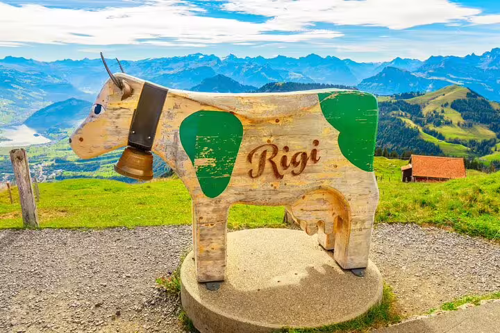 Wooden cow sculpture with 'Rigi' inscription overlooking scenic Swiss Alps landscape.