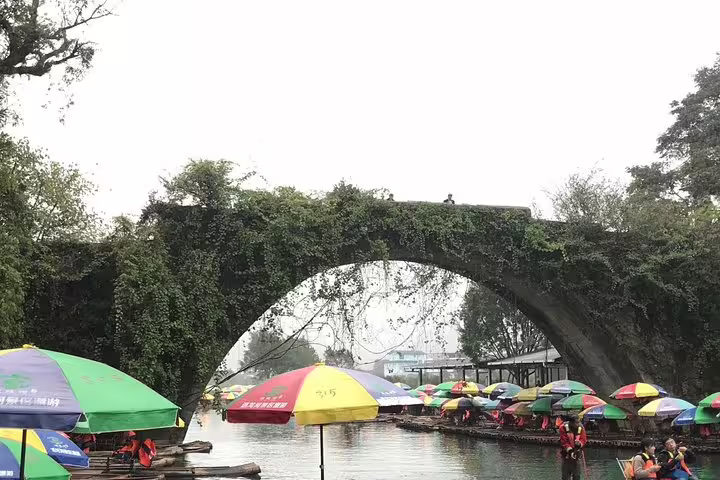 Colorful bamboo rafts under an ancient stone bridge on the Xingping River during a Yangshuo day tour.