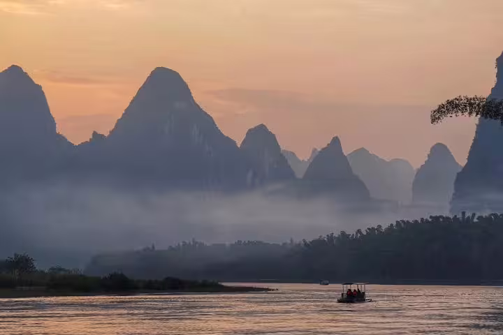 Boat gliding on the Li River at sunset with misty karst peaks in Xingping, ideal for a scenic Yangshuo tour.