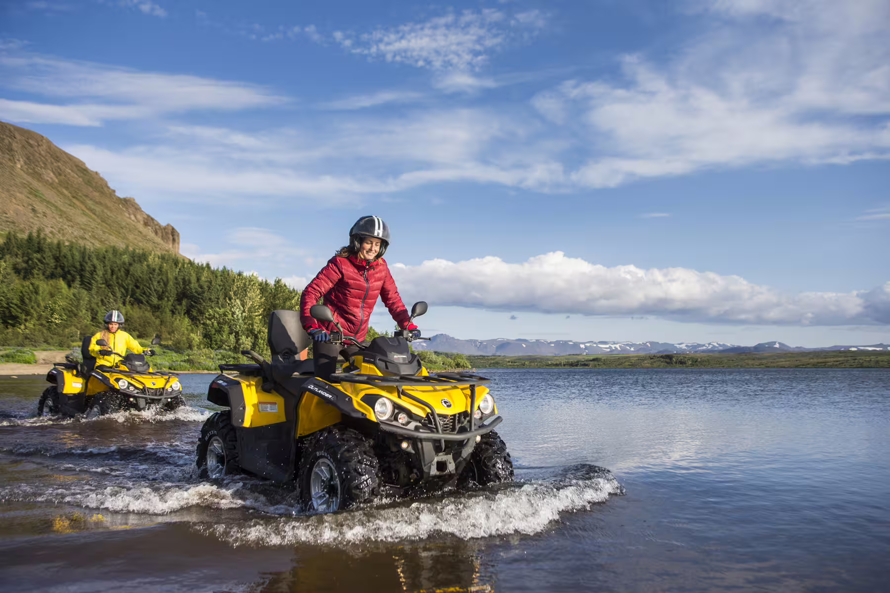 Adventurers ride yellow ATVs through a scenic river landscape under blue skies, perfect for an exciting ATV and whale watching tour.