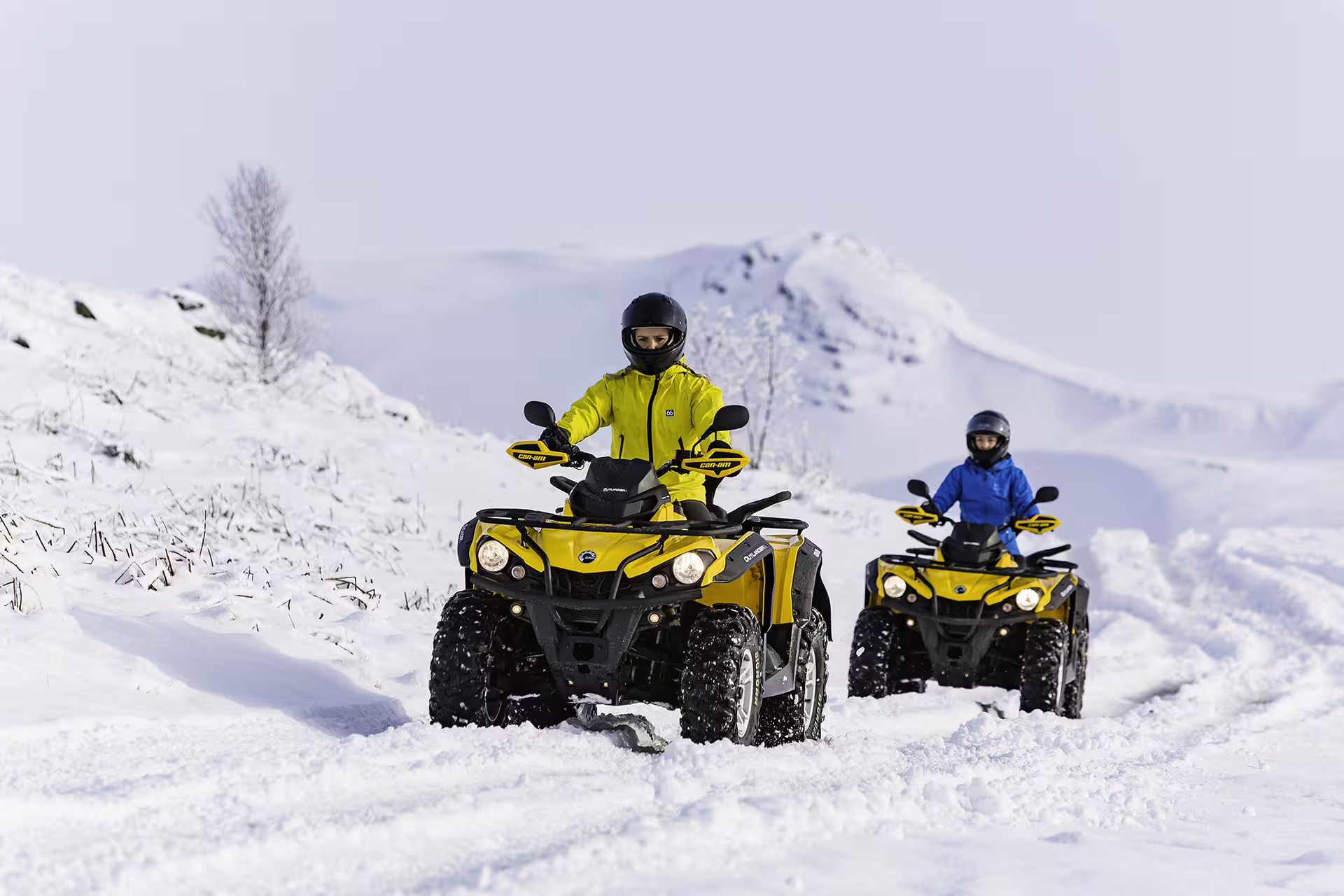 Two people ride yellow ATVs through snowy terrain, highlighting adventure and excitement in a wintery outdoor tour experience.