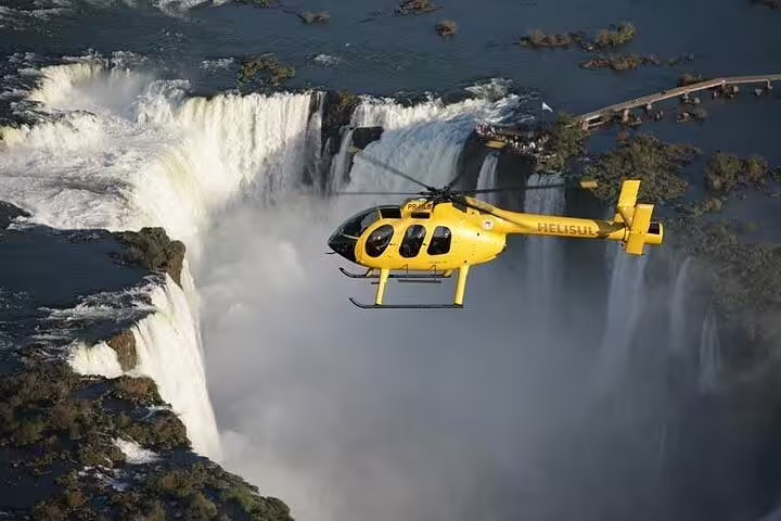 Yellow helicopter flying over Iguazu Falls, offering a stunning panoramic view of cascading waterfalls and lush surroundings.