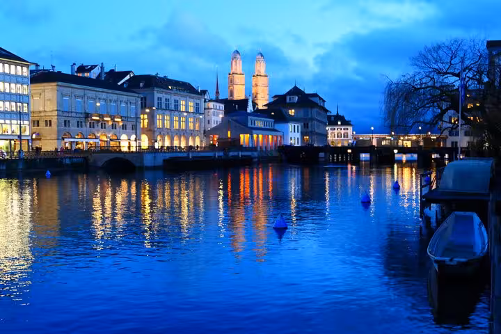 Evening view of Zurich's illuminated old town reflecting on the Limmat River, showcasing city charm.