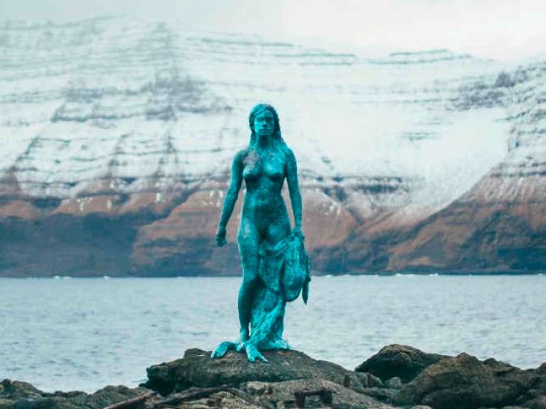 In Mikladalur, the Seal Woman Statue in bronze captures a Faroese legend: a woman, in traditional dress, holding a seal pup, symbolizing her transformation between seal and human forms.