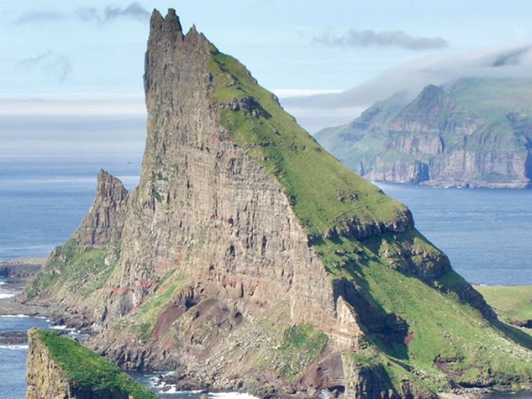 Tindhólmur is a small islet located off the western coast of the island of Vágar in the Faroe Islands. It is one of the most photographed and iconic landmarks of the Faroe Islands, known for its dramatic and rugged appearance.