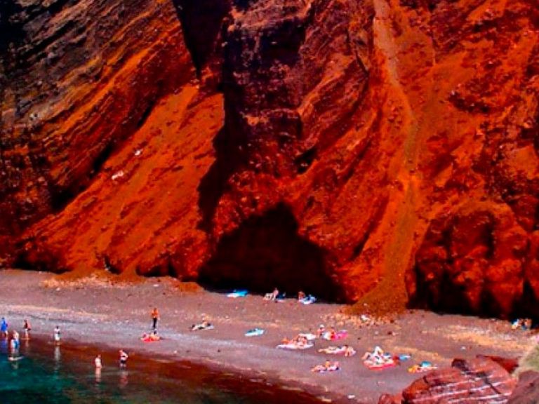 Red Beach, Santorini, mesmerizes with its vibrant hue, courtesy of the towering volcanic cliffs surrounding it. A result of an ancient volcanic eruption, this captivating coast is an awe-inspiring Greek treasure.
